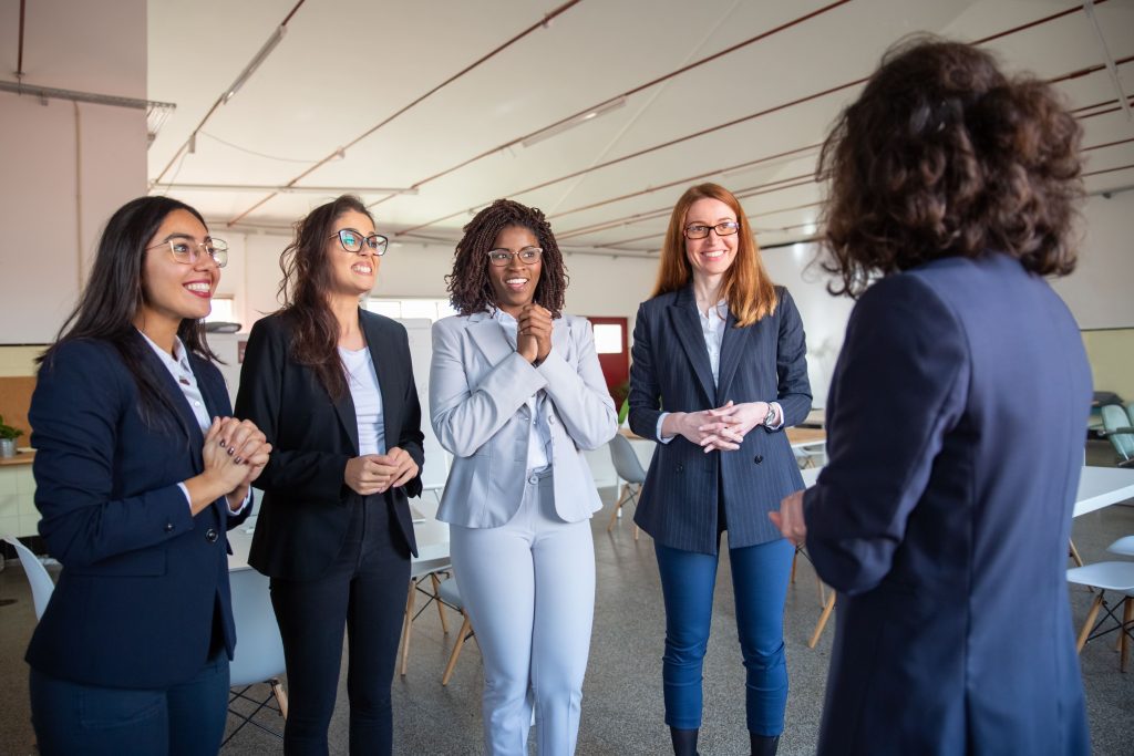 Femme prenant la parole dans une réunion, posture engagée et regard assuré, les autres écoutent attentivement